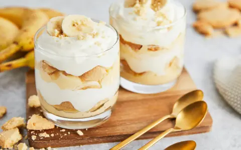 Zwei Gläser mit cremigem Bananenpudding, geschichtet mit Keksen und Bananenscheiben. Ein köstliches Bananenpudding Rezept zum Nachmachen.