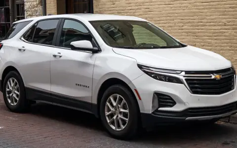 Biały Chevrolet Equinox, wszechstronny chevrolet suv, zaparkowany na brukowanej ulicy przed ceglanym budynkiem.