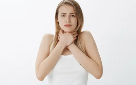 Młoda kobieta zaniepokojona, trzymająca się za gardło, jakby czuła flegmę w gardle po jedzeniu.