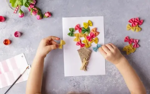 Dziecko tworzy bukiet z kolorowego makaronu farfalle na laurce. Świetne pomysły na laurki!
