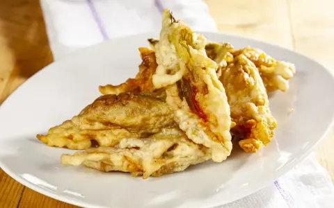 Fiori di zucca fritti dorati e croccanti su un piatto bianco, pronti per essere gustati.