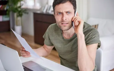 Zmartwiony mężczyzna z dokumentami w ręku rozmawia przez telefon, martwiąc się o niespłacony kredyt odnawialny.
