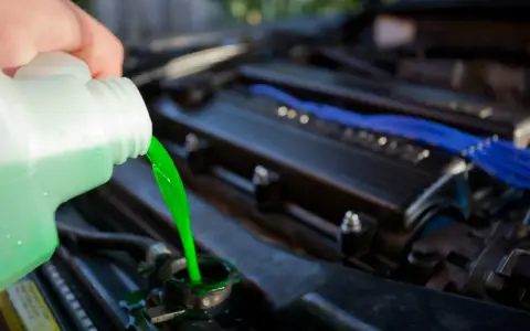 A hand pours bright green coolant into a car's radiator. This prevents the engine from overheating, unlike if coolant were mixed with oil.