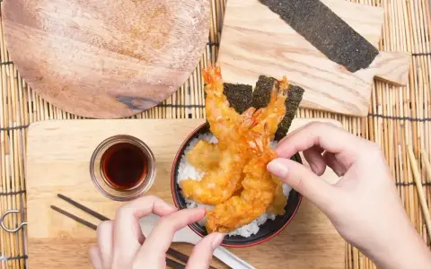 Ręce układają chrupiące krewetki tempura na ryżu. Idealny przepis na tempurę do domowego obiadu.