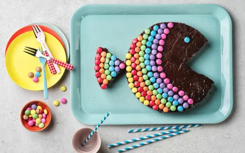 Gâteau en forme de poisson, décoré de Smarties formant un arc-en-ciel. Un œil bleu et une bouche ouverte complètent ce délice coloré.