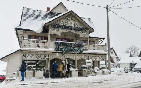 Drewniana chata z napisem "Schronisko Smaków" i neonem "Restauracja" w Bukowinie Tatrzańskiej, otoczona śniegiem.