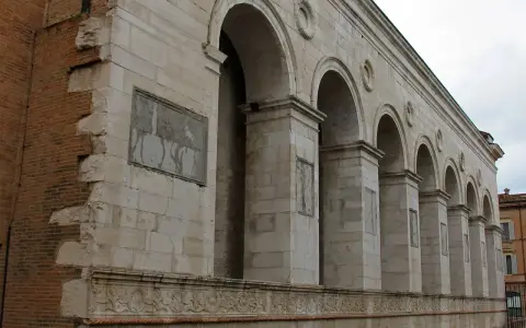Archi maestosi e decorazioni in pietra della chiesa San Francesco a Rimini, con un muro in mattoni a vista che racconta la sua storia.