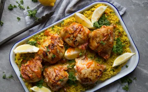 Poulet piri piri savoureux sur un lit de riz jaune, garni de quartiers de citron et de persil frais. Un délice épicé à partager.