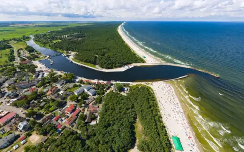 Widok z lotu ptaka na miasteczko nad zatoką, las i plażę. Na falochronie widać czerwoną latarnię morską kikut.