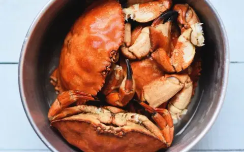 Un cuenco metálico lleno de buey de mar cocido, con sus caparazones anaranjados y pinzas visibles.