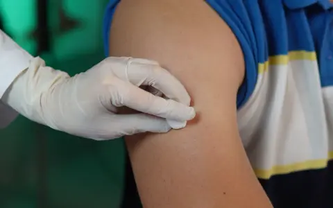 Ręka w rękawiczce dezynfekuje ramię przed podaniem zastrzyku. To przygotowanie do iniekcji śródskórnej.