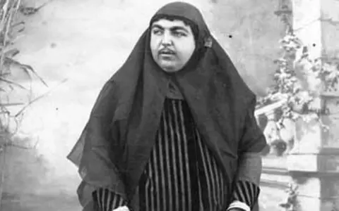 Zahra Khanom Tadj es-Saltaneh, księżniczka perska, w czarnym hidżabie i pasiastym stroju, pozuje na tle ogrodu.