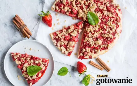 Pyszna tarta z truskawkami i kruszonką, udekorowana miętą, obok laski cynamonu i świeżych truskawek.