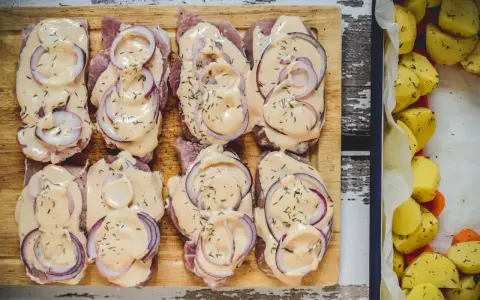 Schab pieczony w plastrach, polany kremowym sosem i posypany ziołami, obok pieczone ziemniaki.