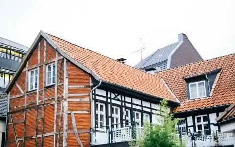 Tradycyjna **konstrukcja muru pruskiego** z ceglanymi wypełnieniami i drewnianymi belkami, obok nowoczesnych budynków.
