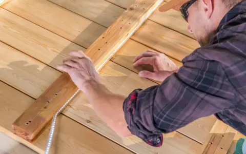 Un homme installe un ruban LED sur une structure en bois. Il réfléchit à quel ruban LED choisir pour son projet d'éclairage extérieur.