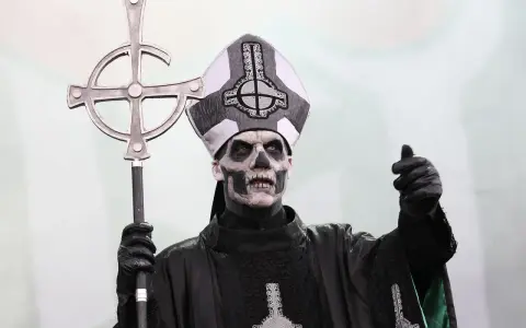Tobias Forge som Papa Emeritus IV, med sin ikoniska sminkning och påvehatt, håller en korsstav. Han påminner om en kuslig onkel Kånkel.