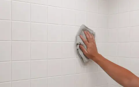 Mano limpiando azulejos blancos recién colocados con un paño gris.