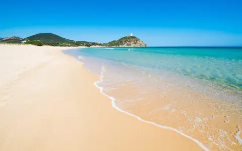Piękne plaże Cagliari z turkusową wodą i piaszczystym brzegiem. W oddali widać wzgórze z wieżą.