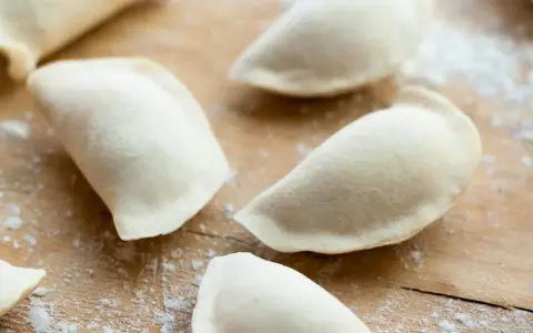 Surowe pierogi na drewnianej desce, przygotowane z ciasta na pierogi bez jajka.