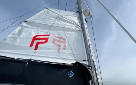Voile blanche avec logo rouge, prête à naviguer à la voile sous un ciel bleu.