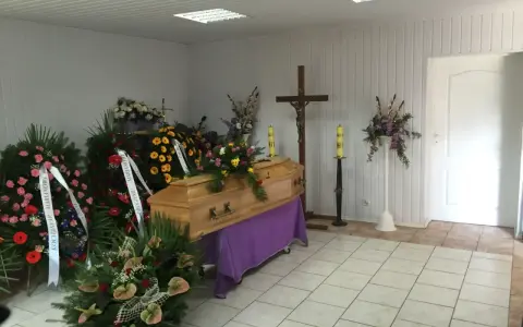 Drewniana trumna otoczona wieńcami i bukietami. Piękne kwiaty na trumnę tworzą smutną, ale uroczystą atmosferę.