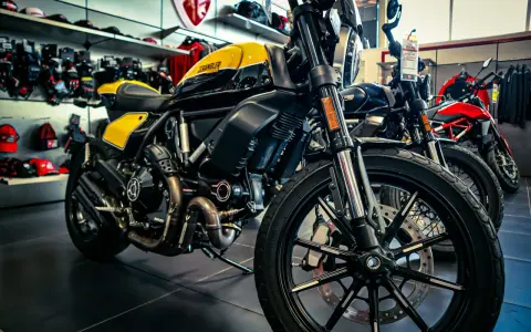 Ducati Scrambler gialla e nera, pronta per i raduni moto. Dietro, altre moto e abbigliamento tecnico.