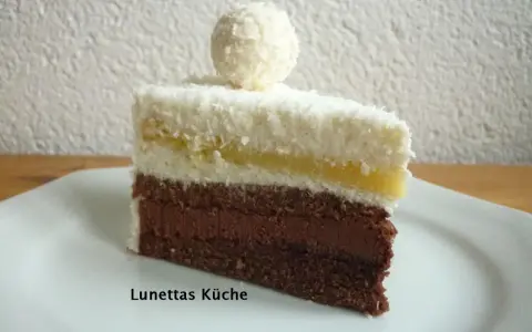 Ein Stück Schoko Kokos Torte mit Kokosraspeln und einer Praline obendrauf.