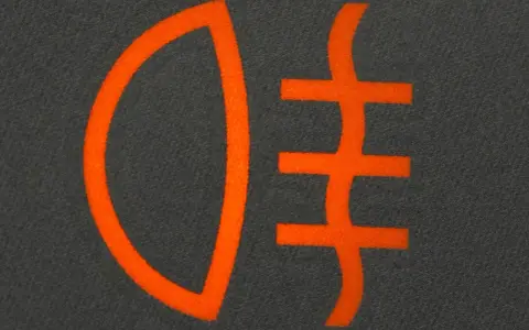 Pomarańczowy symbol świateł mijania na ciemnoszarym tle. Ikona przedstawia reflektor z trzema poziomymi liniami.