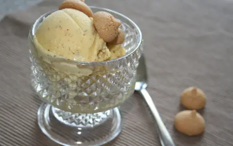 Ein Glas mit cremigem Marzipan Eis, garniert mit kleinen Keksen. Daneben liegen zwei weitere Kekse und ein Löffel.