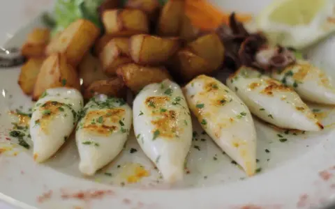 Chipirones a la plancha, tiernos y dorados, acompañados de patatas rústicas y un toque de perejil fresco.