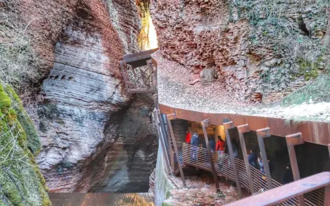 Un orrido ponte alto attraversa una gola rocciosa, con persone che salgono una scalinata metallica.
