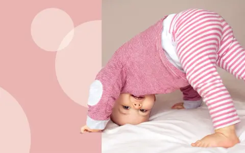 Uśmiechnięte dziecko w różowo-białe paski, kiedy dziecko raczkuje, wywraca się do góry nogami na białym tle.