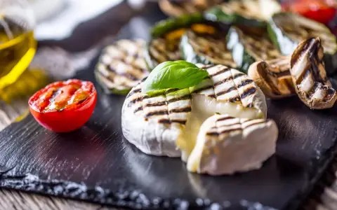 Grillowany camembert z pomidorkiem, cukinią i pieczarkami na czarnej desce.