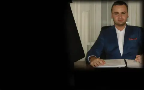 Mężczyzna w garniturze siedzi przy biurku z dokumentami.