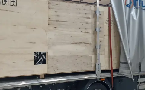 Drewniana skrzynia z widocznym fragmentem felgi, gotowa do transportu. Widać logo firmy transportowej i oznaczenia towaru.