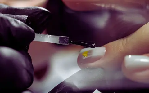 Application d'un vernis transparent sur un ongle orné d'un petit cœur jaune. Le base coat, c'est quoi ? C'est la première étape pour une manucure parfaite.