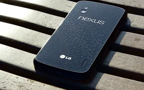 Ciemny tył telefonu LG Nexus 4 z kroplami wody na powierzchni, leżący na drewnianej ławce.