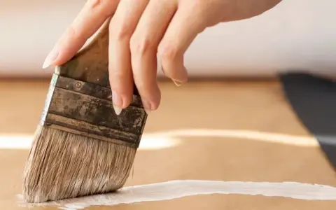 Main d'une personne appliquant une couche de primaire sur du mdf avec un pinceau.