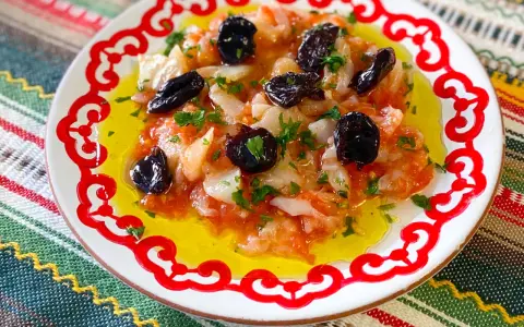Esqueixada de bacalao con aceitunas negras y perejil, servida en un plato blanco con borde rojo sobre un mantel colorido.