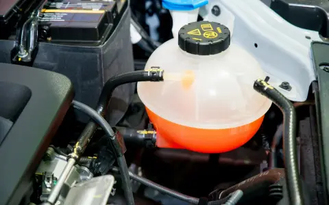 A car's coolant reservoir, showing the orange fluid level. This helps determine how much coolant does a car take.