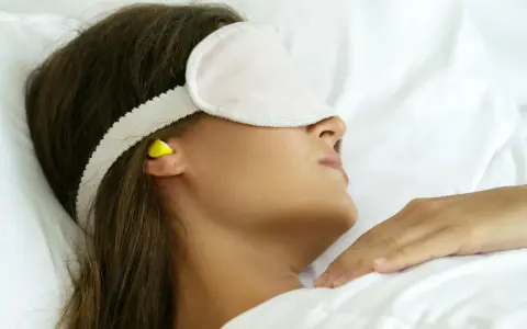 Femme dormant avec un masque et des boules quies pour éviter le bruit, utile en cas d'otite ou pour un sommeil paisible.