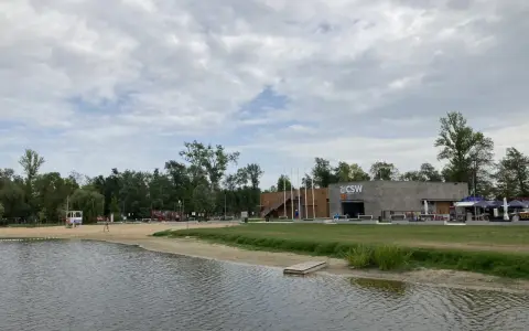 Spokojne jezioro małe żnińskie z piaszczystą plażą, budynkiem CSW i zielenią w tle.