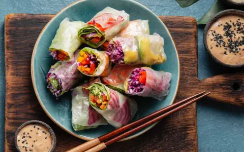 Assiette de rouleaux de printemps colorés, remplis de légumes frais et servis avec une sauce tahini.