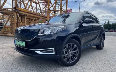 Czarny, lśniący SUV, jeden z chińskich samochodów elektrycznych, zaparkowany obok żółtej konstrukcji budowlanej.