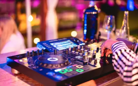 Main d'un dj house connu manipulant la console, lumières vives et ambiance festive.