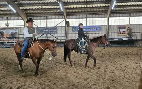 Mann mit Hut und ein Jugendlicher üben Reining Reiten in einer Reithalle.
