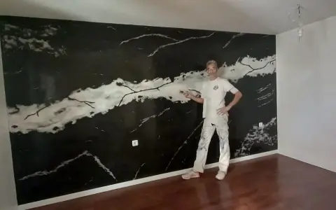 Pintor posa frente a una pared con falso estuco de mármol negro y blanco.