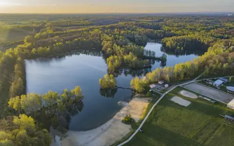 Malownicze jezioro Czechowice otoczone zielonym lasem, z piaszczystą plażą i zabudowaniami rekreacyjnymi.