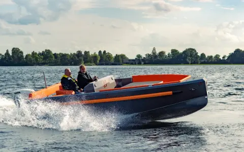 Deux hommes naviguent sur un bateau rapide, créant des éclaboussures. Le design moderne du bateau, avec ses accents orange vif, suggère une conception soignée, peut-être pour fabriquer des flaps pour bateau.